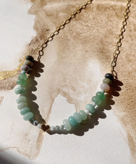 Necklace with green and blue gemstones on a textured beige background